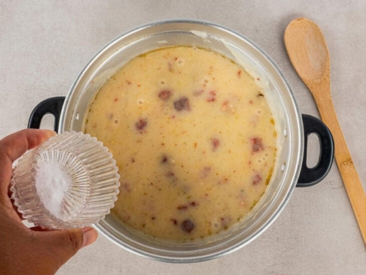 Creme de mandioca sendo incorporado à panela e temperado com sal enquanto é mexido.