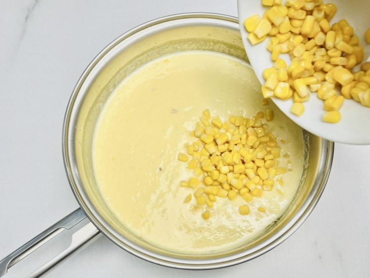 Na panela, a mistura do liquidificador adicionada, o milho sendo acrescido também.