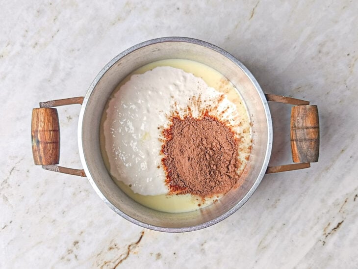 Leite condensado, creme de leite e chocolate em pó sendo adicionados à panela.