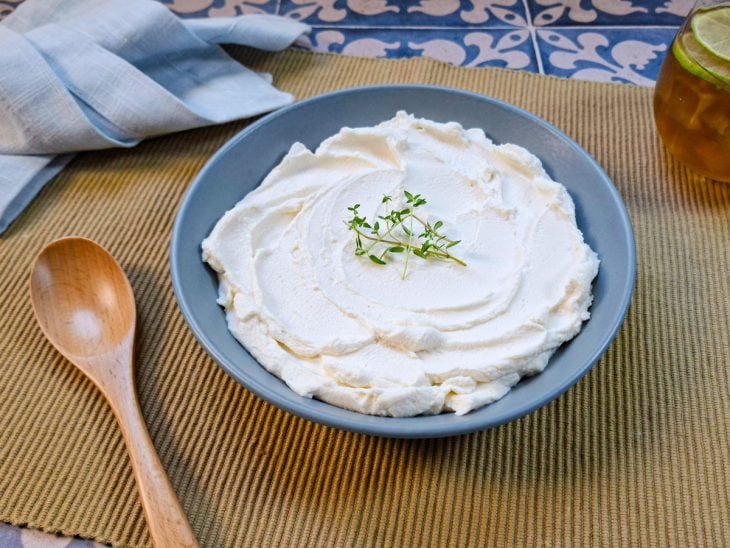 Creme de ricota servido num recipiente redondo azul e finalizado com ervas.
