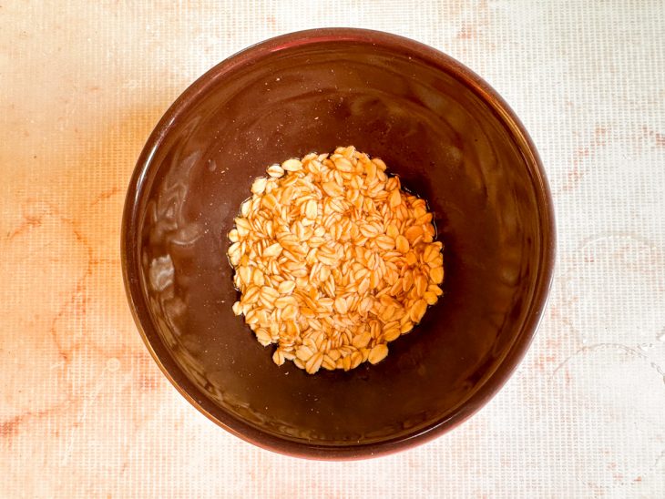 Aveia em flocos hidratando com água morna em uma tigela antes do preparo da massa.