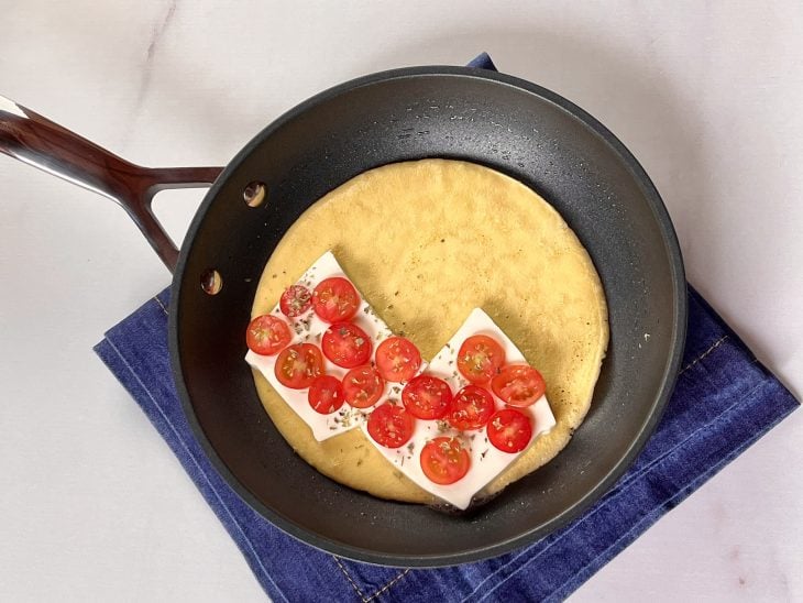 Uma frigideira com a massa da crepioca recheada com queijo, tomate e orégano.