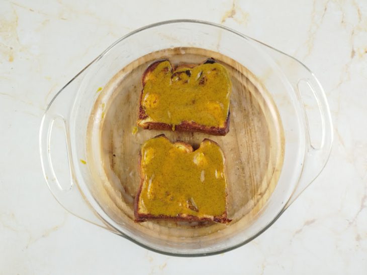 Camada de mostarda sobre as fatias de pão.