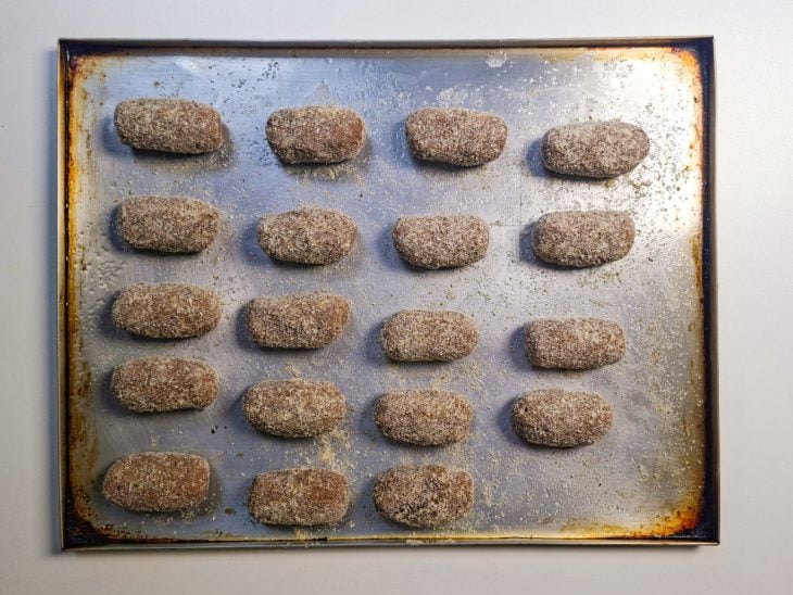 Croquetes modelados sendo empanados na farinha de rosca.