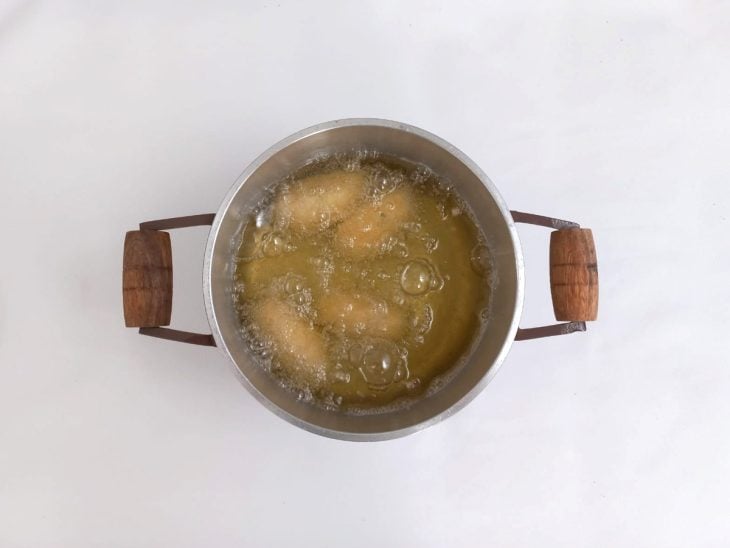 Uma panela com óleo e croquetes fritando.