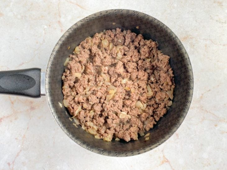 Uma panela com azeite, alho, cebola, carne moída e temperos.