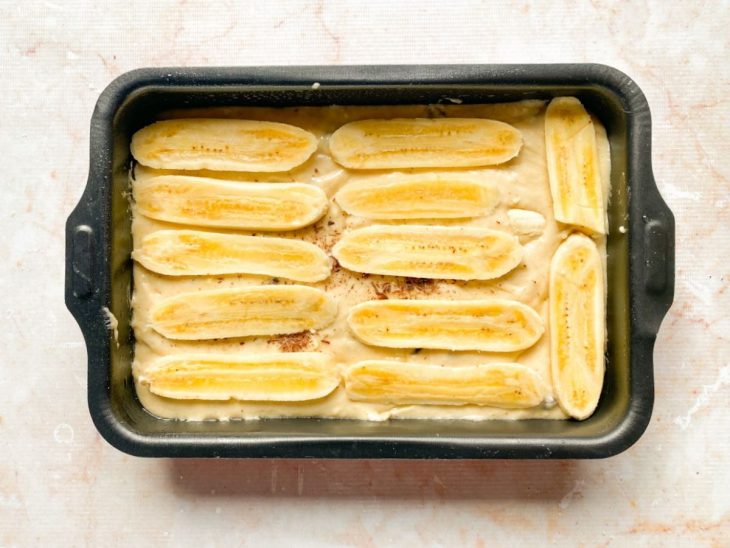 Massa transferida para uma forma e bananas fatiadas adicionadas sobre a massa.