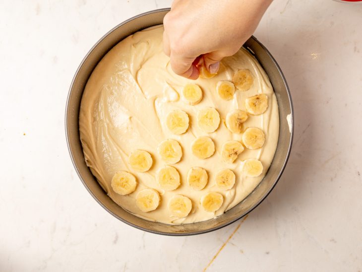 Rodelas de banana posicionadas sobre a massa na forma.