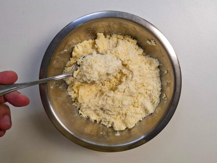 Ingredientes da farofa sendo misturados com as pontas dos dedos até formar uma textura soltinha e granulada.