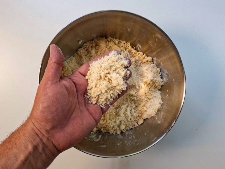 Ingredientes da farofa sendo misturados com as mãos até formar textura granulada.