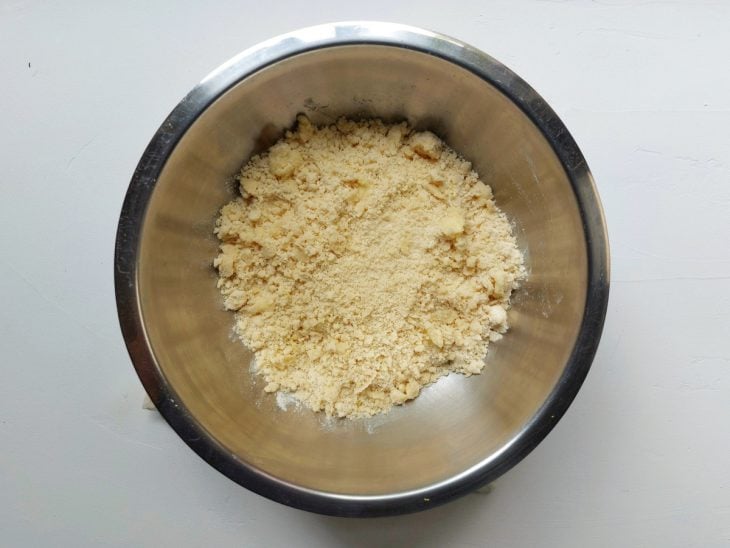 Um recipiente contendo uma farofinha de farinha de trigo, açúcar, manteiga e sal.