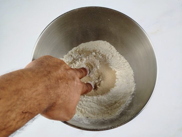 Farinha e fermento biológico misturados com os dedos em uma tigela.