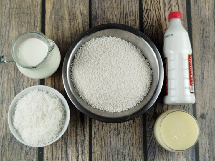 Ingredientes organizados na bancada com tapioca granulada, leites e coco ralado dispostos em recipientes.