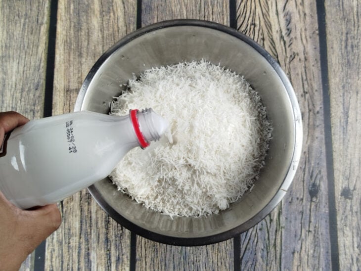 Tapioca granulada, coco ralado e leite de coco sendo misturados com uma colher em uma tigela grande.
