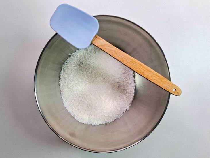Tapioca granulada, sal, açúcar e coco ralado misturados em uma tigela.