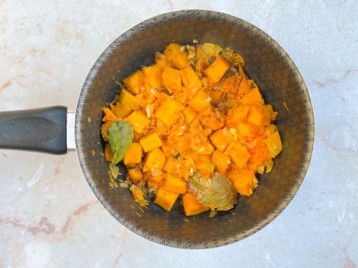 Cebola, cenoura, abóbora e temperos a refogar na panela.