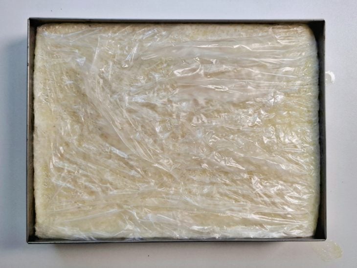 Massa de dadinho de tapioca em um refratário forrado e coberto por plástico filme.