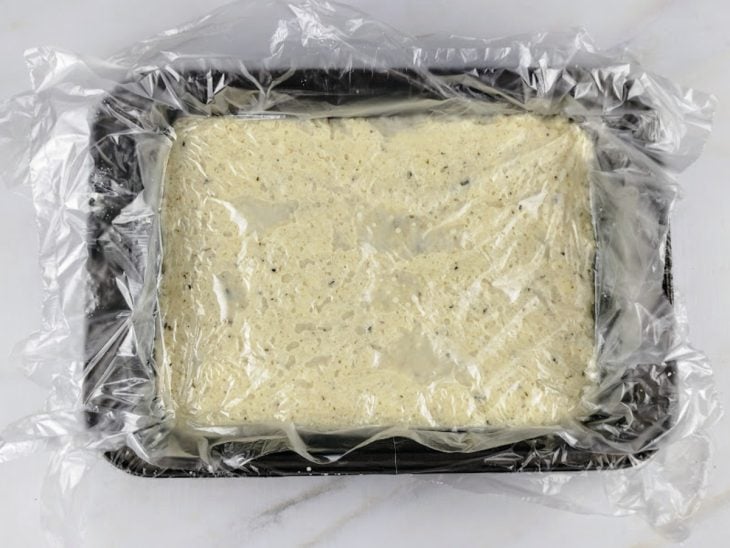 Massa distribuída na assadeira coberta e forrada por plástico de alimentos.