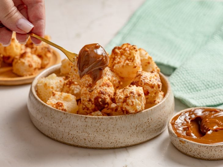 Dadinhos de tapioca prontos para consumo e um deles espetado em um garfo com doce de leite.