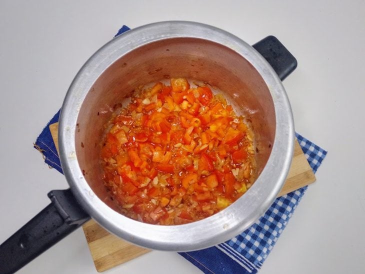 Uma panela de pressão contendo cebola, alho e tomates refogados.