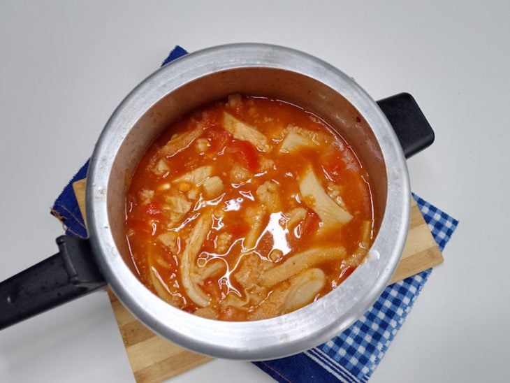 Uma panela de pressão contendo cebola, alho, tomates, bucho, feijão-branco e molho de tomate.