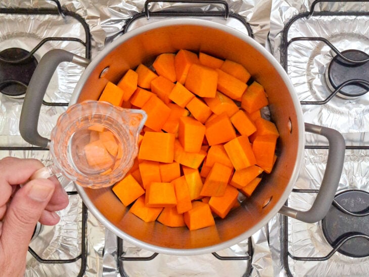 Cubos de abóbora com água, canela em pau e cravos-da-índia dentro de uma panela de fundo grosso.