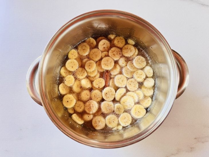 Rodelas de banana, limão, cravo e canela em pau adicionados na panela.