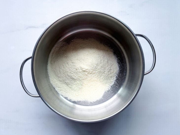 Leite em pó sendo colocado em uma panela e levado ao fogo baixo.