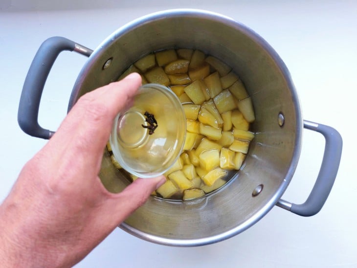 Panela com mamão verde, com cravos sendo adicionados.