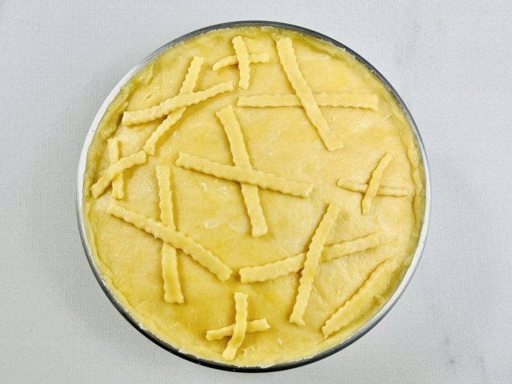 Massa cobrindo o empadão e bordas sendo decoradas com recortes.