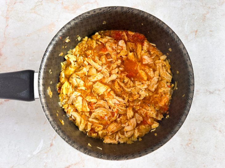 Frango desfiado e temperos incorporados ao refogado.