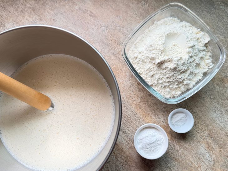 Mistura na tigela, farinha, sal e fermento ao lado.