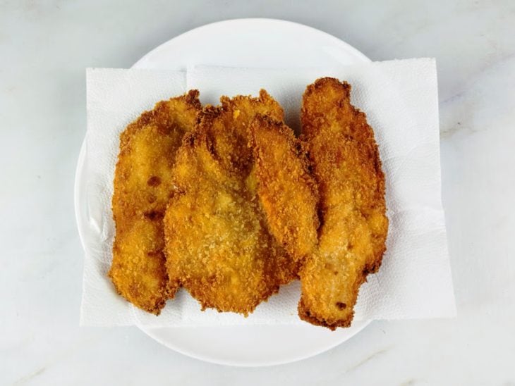 Filés de frango empanados e fritos acomodados em um prato com papel toalha.