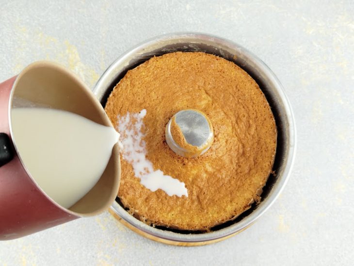 Leite quente sendo regado uniformemente sobre o bolo morno.