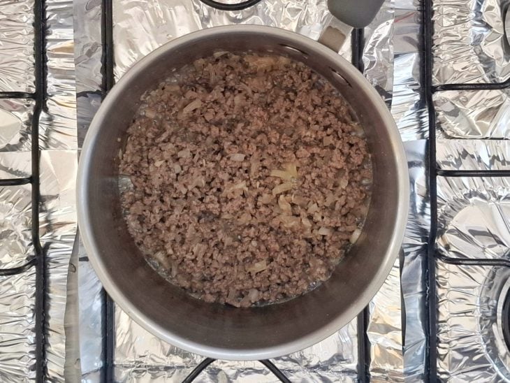 Uma panela ao fogo com cebola, alho, azeite e carne moída.