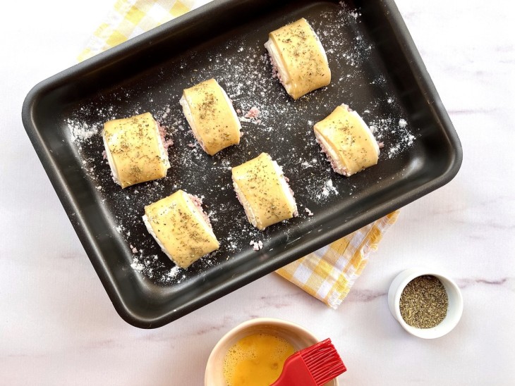 Uma assadeira com enroladinhos de presunto e queijo.