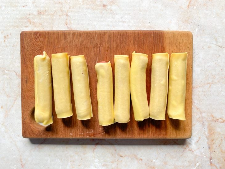 Salsichas enroladas na massa em uma tábua.