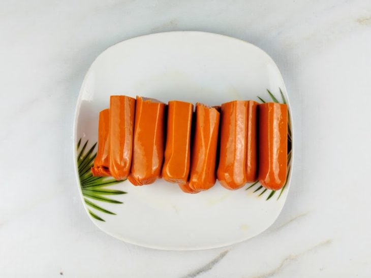 Salsichas cortadas ao meio e reservadas em um prato.