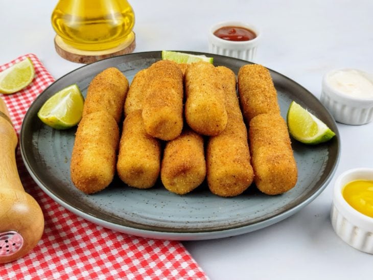Enroladinhos de salsicha simples prontos para servir e acompanhados de molhos e limões.