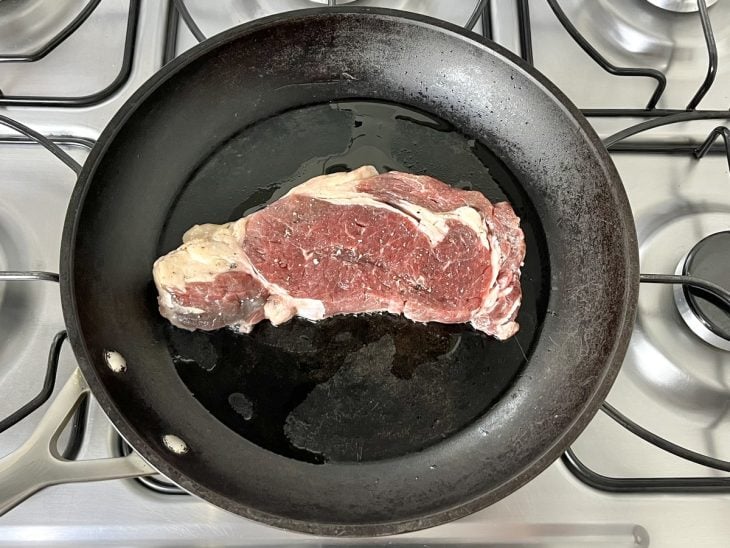 Uma frigideira selando um bife de entrecot.