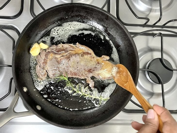 Uma frigideira selando um bife de entrecot com manteiga.