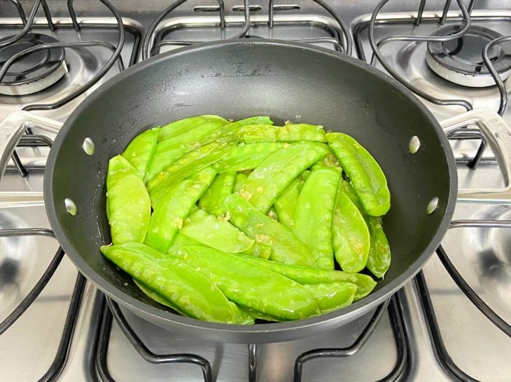 Uma frigideira tampada refogando ervilhas-tortas.