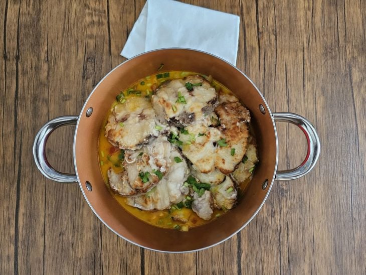 Uma panela cozinhando postas de peixes com vegetais e leite de coco.