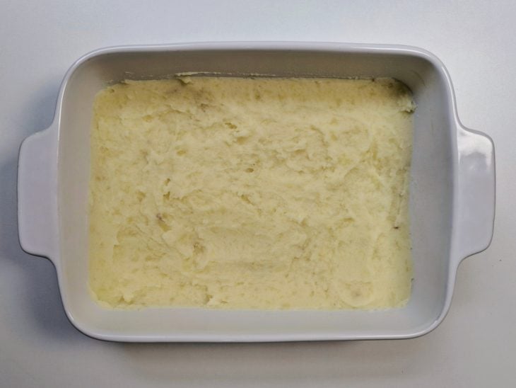 Camada de purê de batata ao fundo de uma travessa.