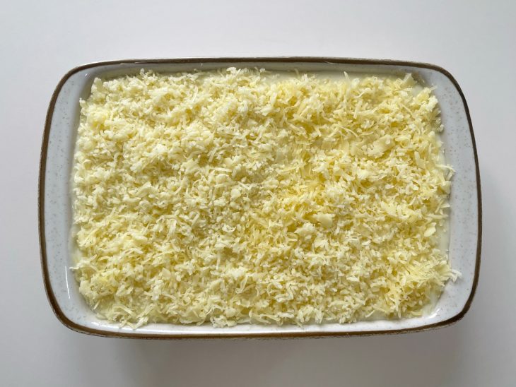 Queijo ralado sendo colocado sobre o escondidinho antes de gratinar.
