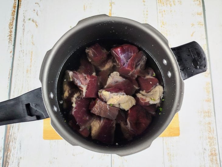 Carne colocada em uma panela de pressão com água.