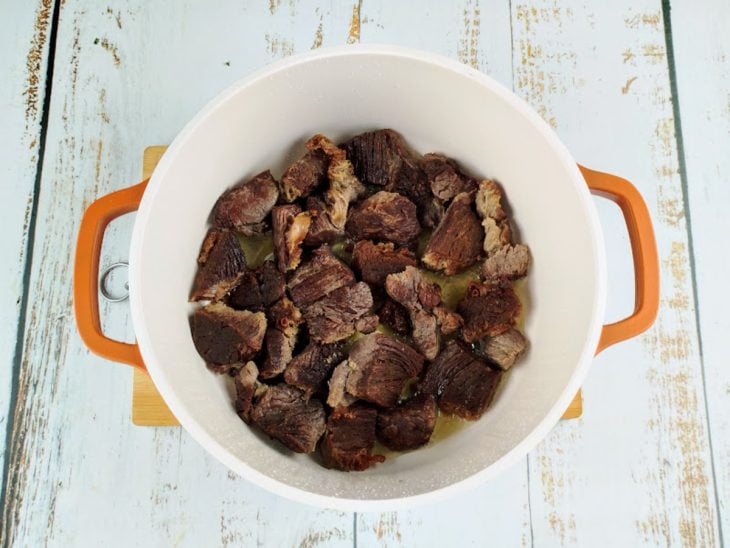 Pedaços de carne colocados em uma panela com óleo.