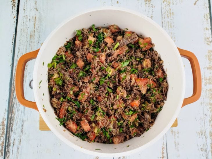 Carne, tomates, coentro e temperos adicionados na panela com cebola e alho refogados.