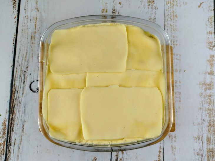 Fatias de queijo acomodadas na superfície para gratinar.