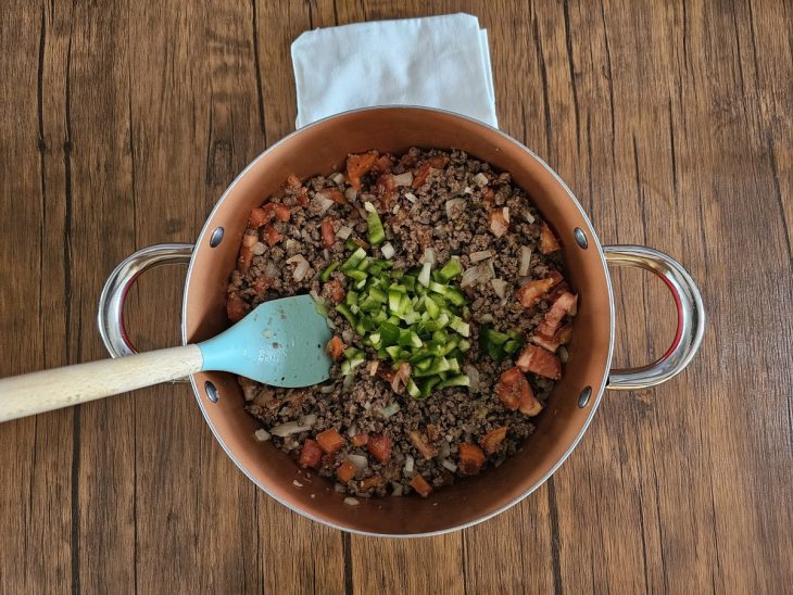 Uma panela contendo carne moída com manteiga, alho, tomate e pimentão.